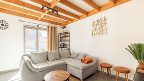 Uma sala de estar moderna com um sofá seccional, uma mesa de madeira redonda e um banquinho pequeno.