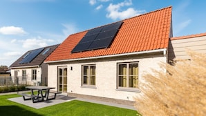 Uma casa moderna com telhado de telhas vermelhas, painéis solares e um gramado bem cuidado.