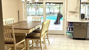Une cuisine équipée d’une table et de chaises, d’un réfrigérateur, et offrant une vue sur une piscine par le biais d’une porte vitrée.