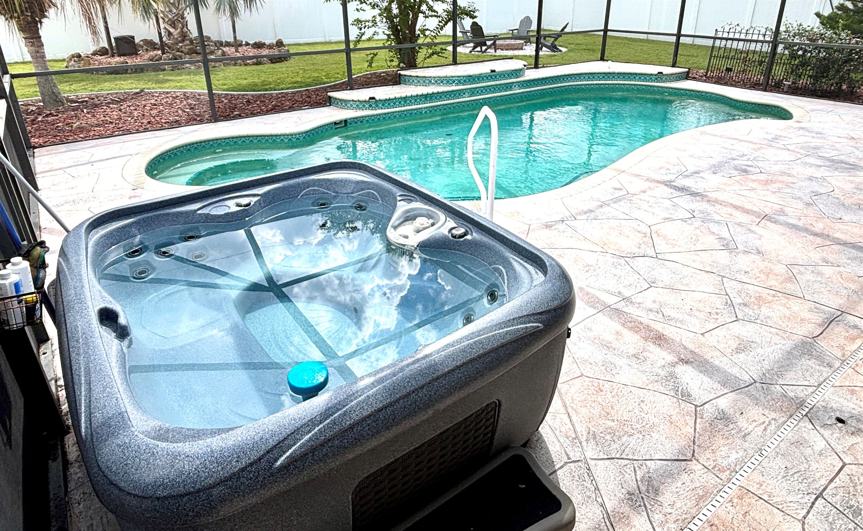 A hot tub with a glass top, surrounded by a stone patio and a swimming pool.