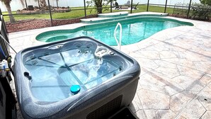 Un bain à remous doté d’un couvercle en verre, entouré d’une terrasse en pierre et d’une piscine.