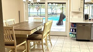 A kitchen with a dining table and chairs, a refrigerator, and a view of a swimming pool through the glass door. - Bring Kids & the Dog! House, Fence + Bunkhouse (Port Charlotte)