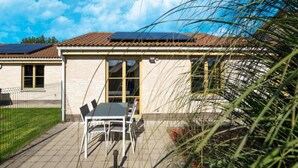 A building with a tiled roof, a fenced patio area with a table and chairs, and solar panels on the roof.