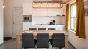 A modern kitchen with white cabinets, a wooden dining table with four chairs, a built-in microwave, and a pendant light fixture.