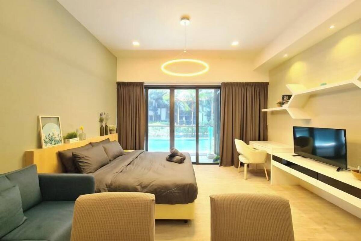 A modern hotel room with a bed, sofa, TV, and a view of the outdoors.