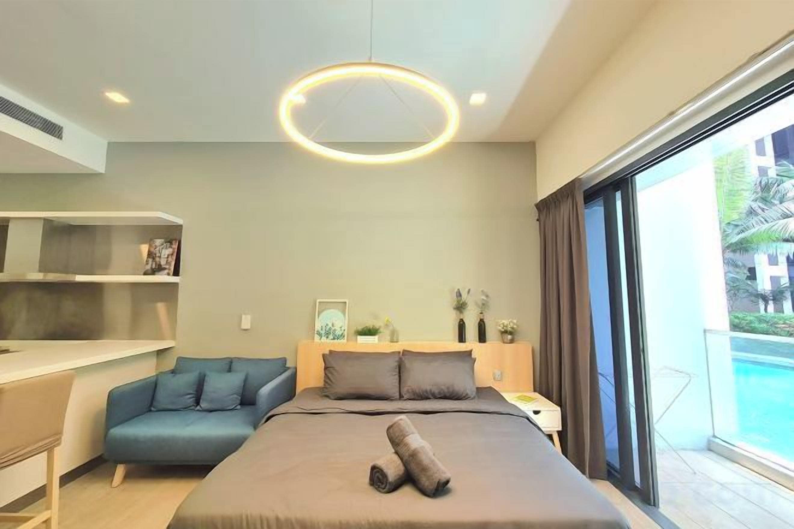 A modern hotel room with a bed, a desk, a sofa, and a view of a swimming pool.