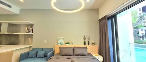 A modern hotel room with a bed, a desk, a sofa, and a view of a swimming pool.