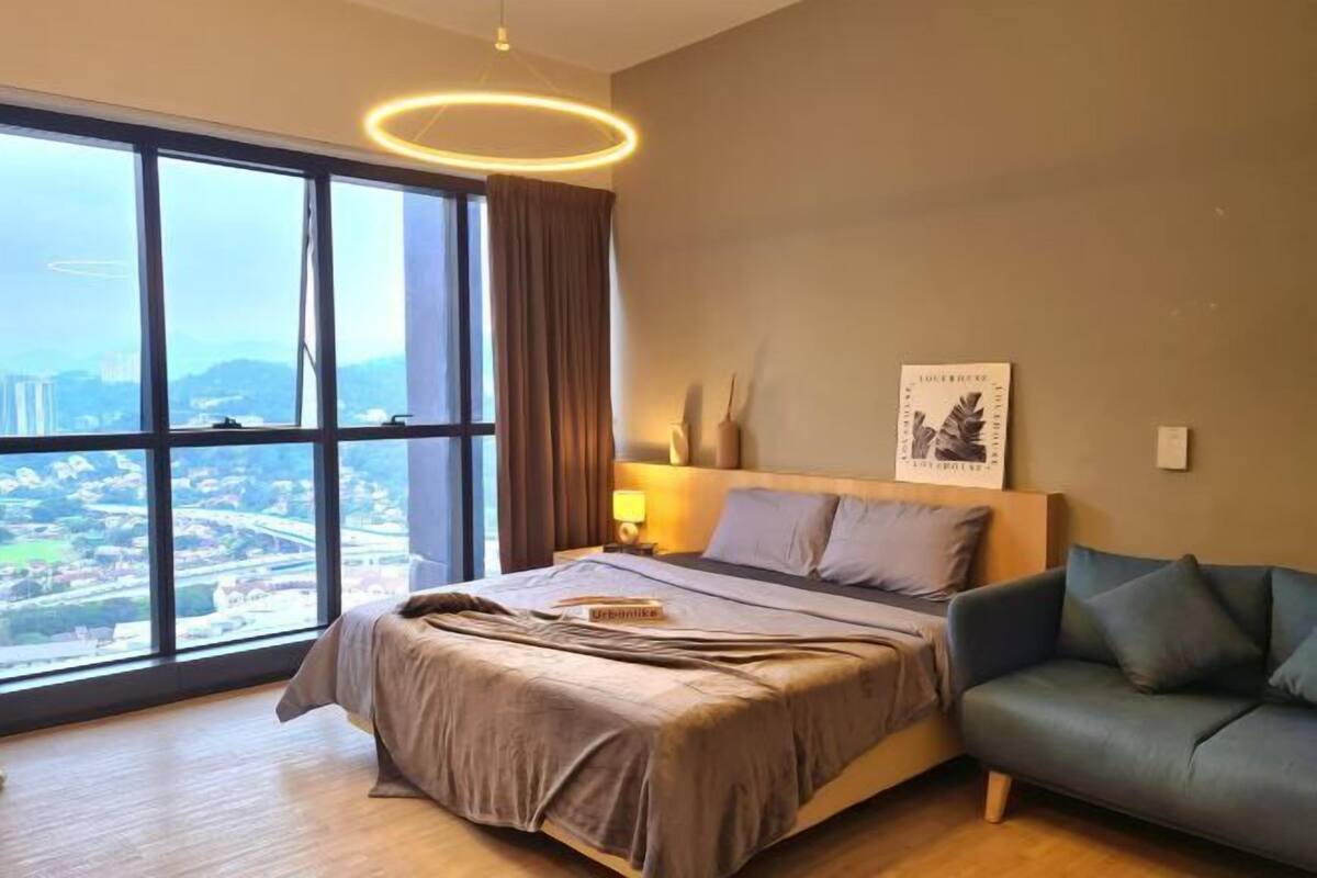 A hotel room with a large window, a bed, a green sofa, and a wall-mounted artwork.