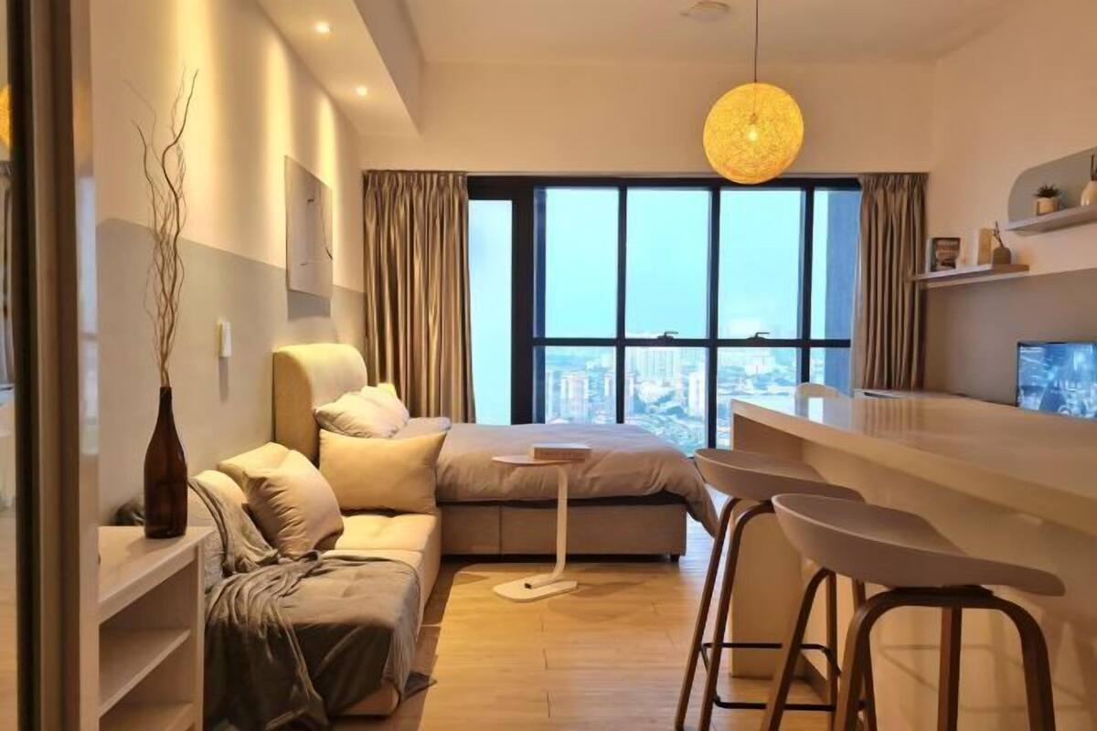 A modern hotel room with a bed, a desk, a bar area, and a view of the city.