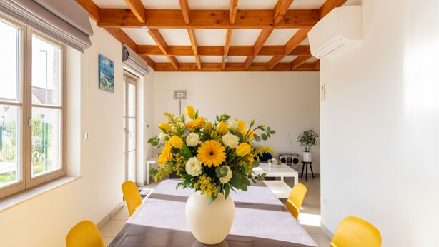 A dining area with a wooden ceiling, a table with a vase of flowers, and yellow chairs. - Contemporary fisher’s house at Westhinder (Koksijde)