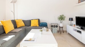 A modern living room with a grey sofa, yellow cushions, a white coffee table, a radio, a television, and a plant. - Contemporary fisher’s house at Westhinder (Koksijde)
