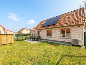 A residential house with a tiled roof, solar panels, a fenced backyard, and a wooden shed.
