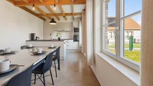 Eine moderne Küche mit Holzbalken, einem Essbereich mit Tisch und Stühlen sowie einem großen Fenster mit Blick auf ein Haus und einen Zaun.