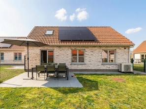 Une maison avec un toit en tuiles, une façade en briques et un patio aménagé avec du mobilier d’extérieur.