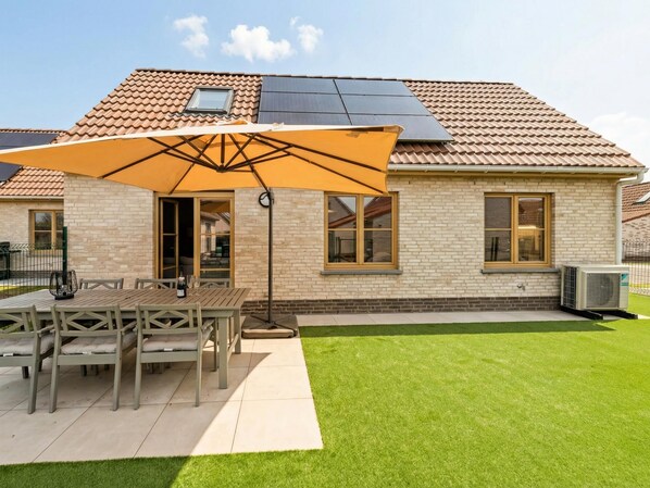 A house with a tiled roof, a brick exterior, a patio with a table and chairs, and a lawn.