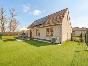 A house with a tiled roof, a solar panel, a lawn, and a fenced yard.