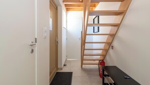 Un couloir étroit avec un escalier en bois, un banc noir et un extincteur.