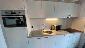 Et moderne køkken med hvide skabe, en stålvask, indbygget ovn og kaffemaskine.