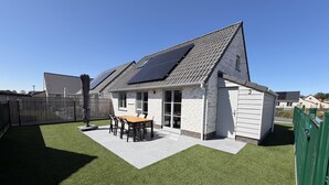 Et hus med skråt tag, solpaneler, en terrasse med bord og stole samt en indhegnet have.