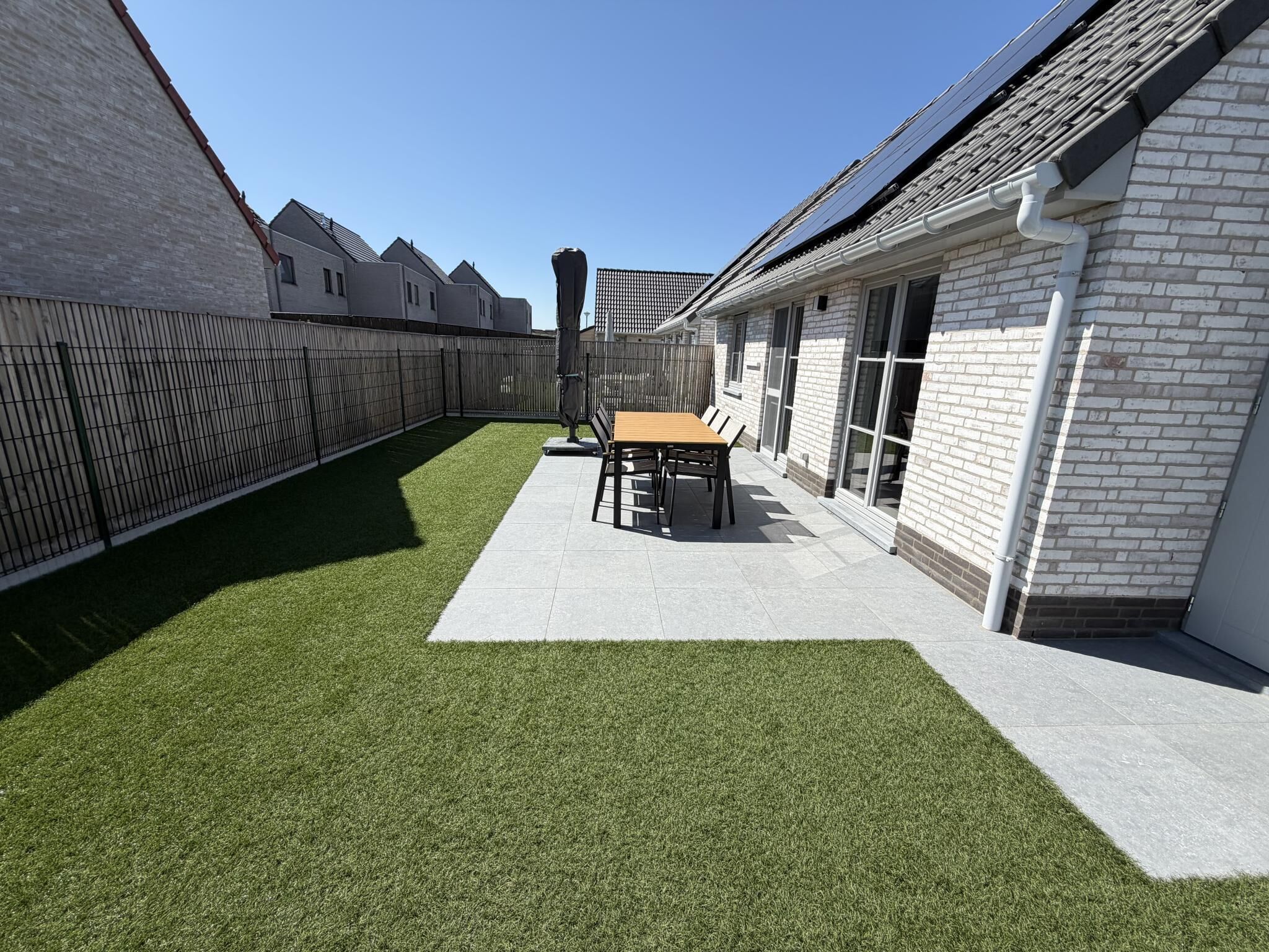 A backyard with artificial grass, a patio table, and a fence.