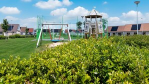 Une aire de jeux avec des balançoires et une structure d’escalade, entourée d’une pelouse et de buissons bien entretenus.
