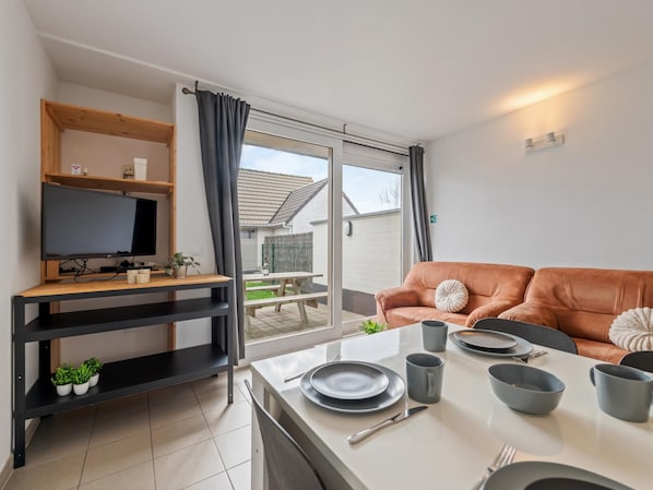 A modern living room with a TV, sofa, dining table, and a view of the outside.