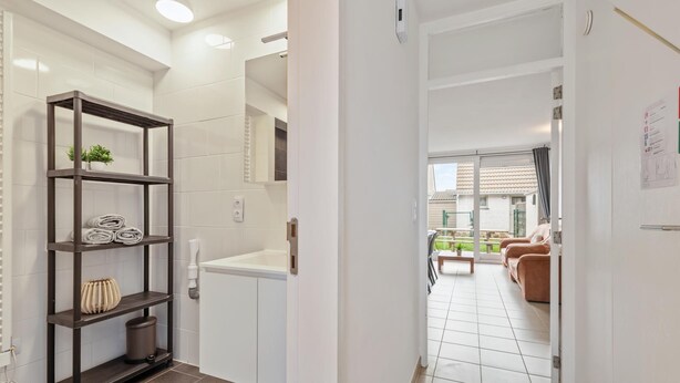 A modern apartment with a hallway leading to a living area, a built-in shelf with towels, and a visible trash bin. - Cosy holiday home on the Westhinder domain (Koksijde)