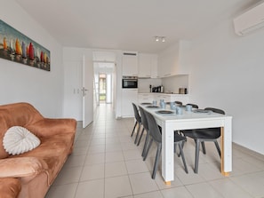 A modern kitchen with white cabinets, a dining table set for four, and a brown leather sofa with a decorative pillow.