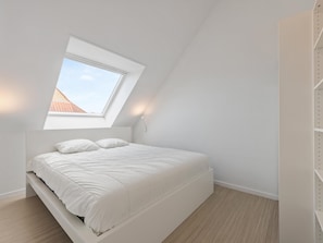 A bedroom with a skylight, a bed, and a white wardrobe.