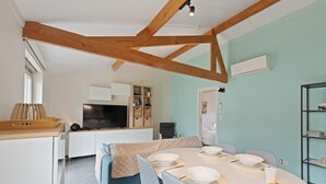 A modern kitchen with a dining area, wooden beams, a TV, and a bookshelf.