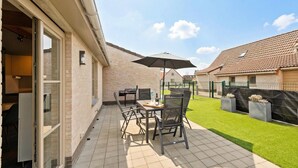 A patio with a table and chairs, a grill, and a lawn.