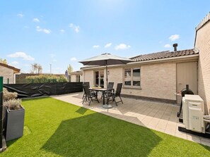 A patio with a table and chairs, a covered umbrella, and a brick house.