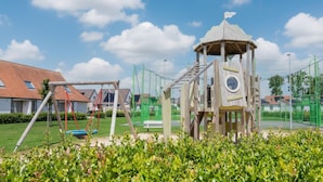 A playground with swings and a climbing structure, surrounded by a fence and greenery. - Pet-friendly holiday home by the coast (Koksijde)