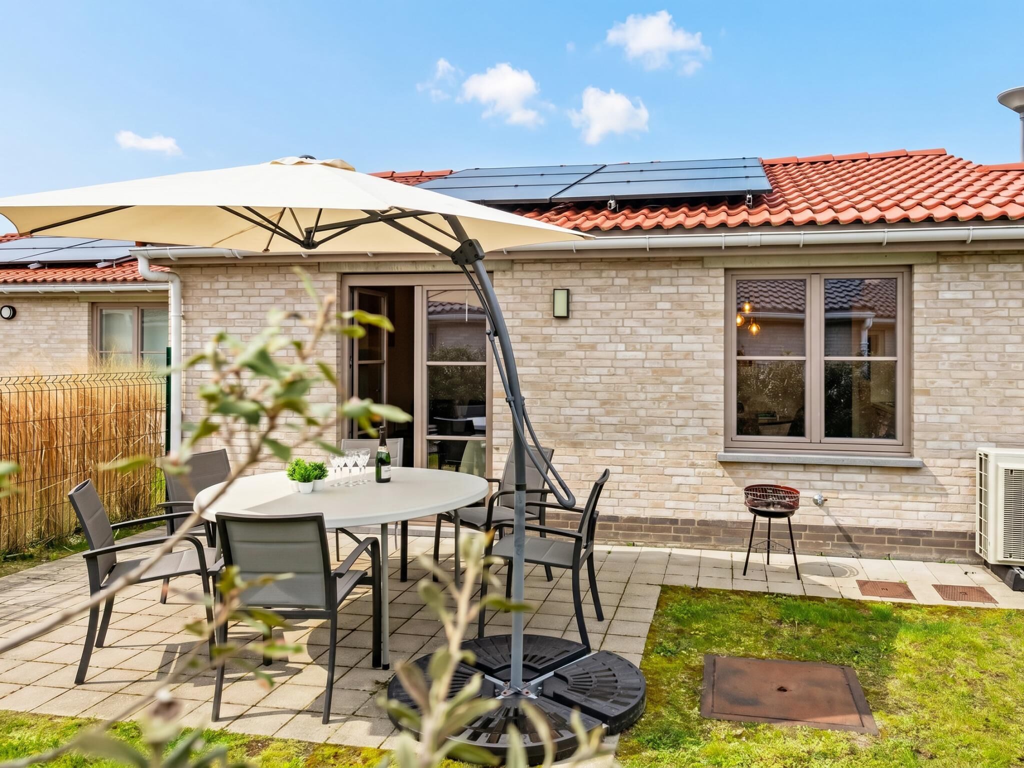 A patio with a table and chairs, a covered umbrella, and a brick house with a tiled roof.