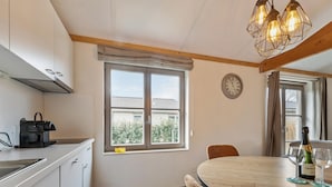 A kitchen with a window, a clock, a table with chairs, and a bottle of wine. - Pet-friendly holiday home by the coast (Koksijde)
