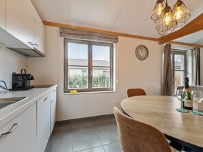 A kitchen with a window, a clock, a table with chairs, and a bottle of wine.