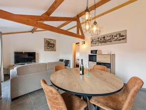 A dining area with a round wooden table, cushioned chairs, a sofa, a television, and artwork on the walls.