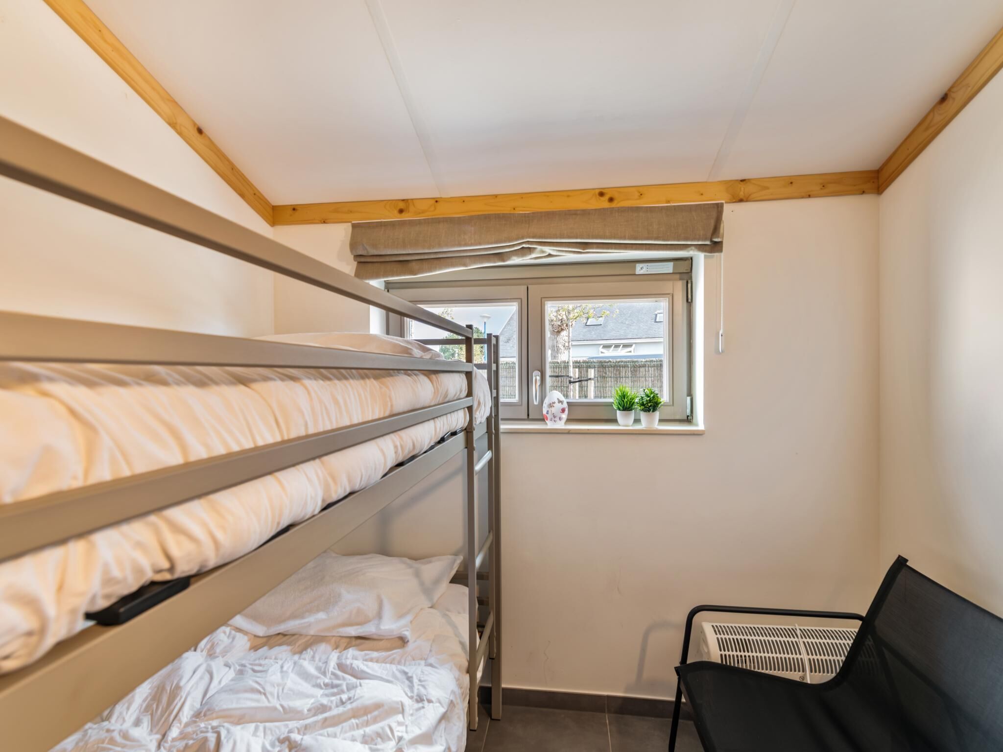 Une chambre avec un lit superposé, une fenêtre, une chaise et un radiateur.