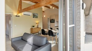 Un interior moderno con vigas de madera a la vista, una zona de comedor con mesa y sillas, y un sofá gris.
