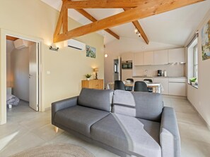 Una sala de estar moderna con un sofá gris, vigas de madera, una cocina con armarios blancos y un comedor.