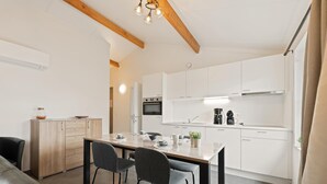 A modern kitchen with white cabinets, a dining table with chairs, and a black leather couch. - Holiday home on park, pets allowed (Koksijde)
