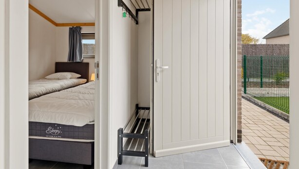 A room with a bed, a bench, and a sliding door leading to an outdoor area. - Holiday home on park, pets allowed (Koksijde)