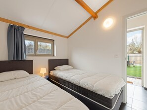 A bedroom with two beds, a window with curtains, a bedside lamp, and a view of the outside. - Holiday home on park, pets allowed (Koksijde)
