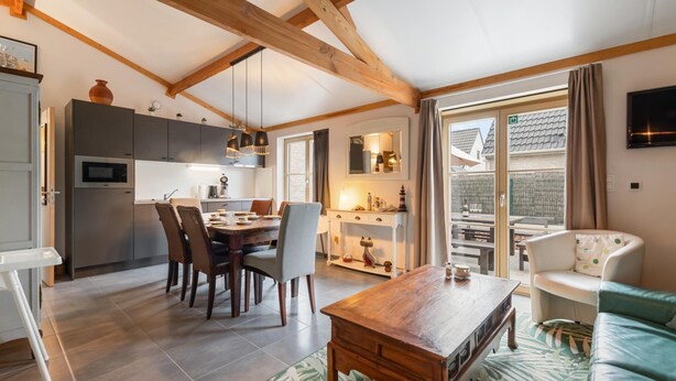 Eine moderne Küche mit Holzbalken, eine Essecke mit Tisch und Stühlen, ein Sofa und ein an der Wand befestigter Fernseher.
