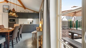 Eine moderne Küche mit dunklen Schränken, ein Essbereich mit Holztisch und -stühlen sowie ein Blick auf einen Garten durch ein großes Fenster.