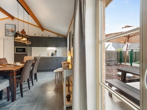 Una cocina moderna con armarios oscuros, una zona de comedor con mesa y sillas de madera, y vistas a un patio trasero a través de un ventanal grande.