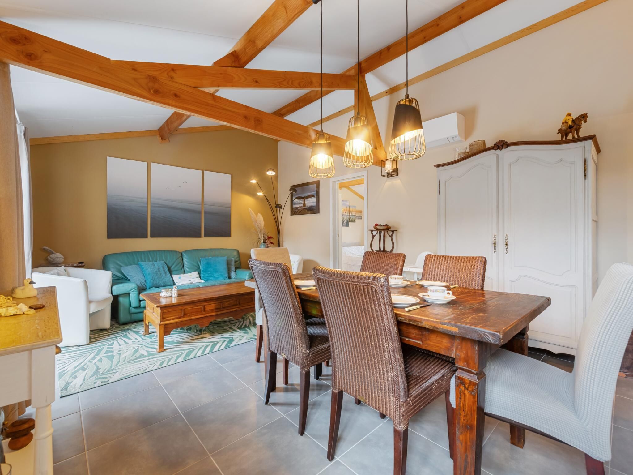 A dining area with a wooden table and wicker chairs, a teal sofa, and a white cabinet.