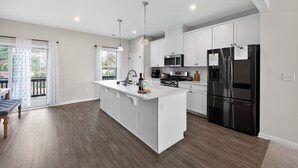 A modern kitchen with white cabinetry, a central island, stainless steel appliances, and a view to the outside. - 
Lux Home - Mins to Downtown, RDU, Fenton, UNC Health, WakeMed, & The Triangle (Cary)