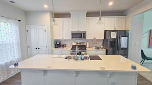 A modern kitchen with a central island, stainless steel appliances, and pendant lighting. - 
Lux Home - Mins to Downtown, RDU, Fenton, UNC Health, WakeMed, & The Triangle (Cary)