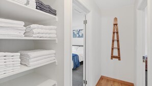 Een hotelkamer met netjes opgestapelde witte handdoeken op planken, een houten ladder aan de muur en een bed met een blauwe deken.